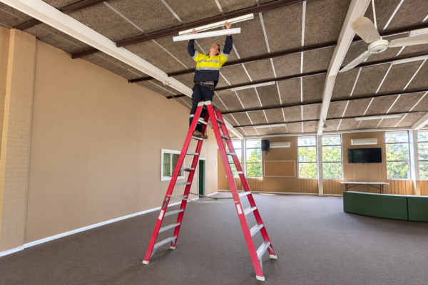 Powellect electrician installing ceiling lighting from a ladder inside a commercial building